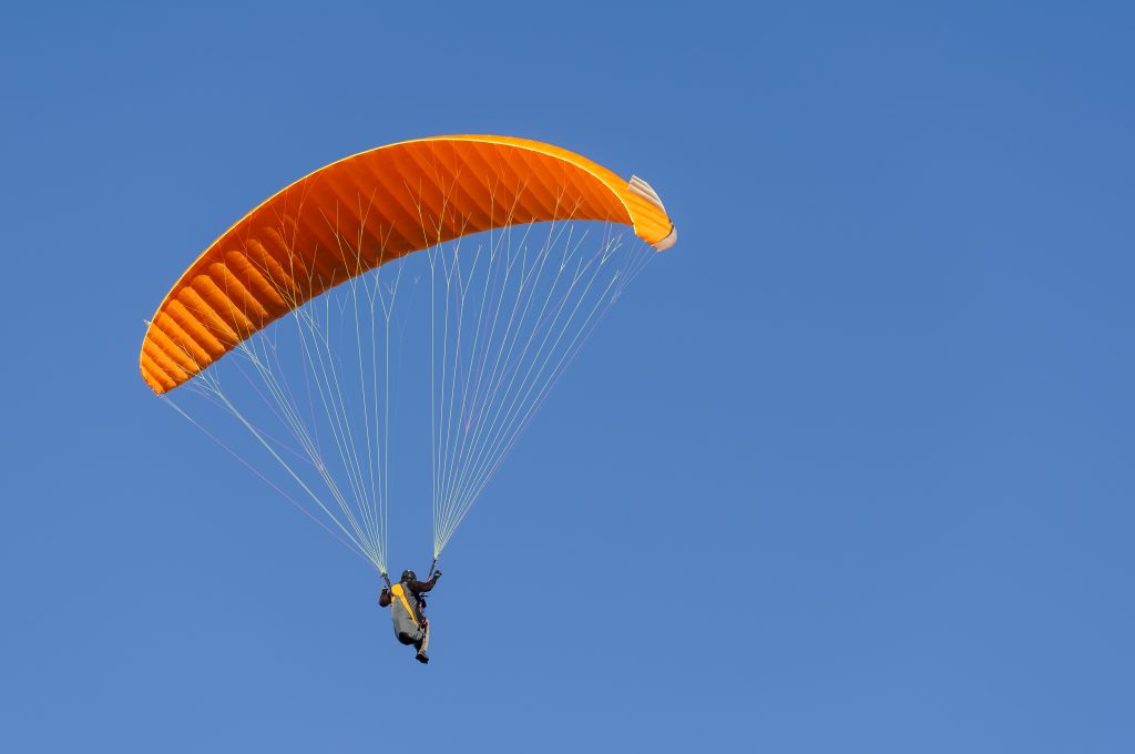 paragliding orange flying against blue sky. adventure sport.